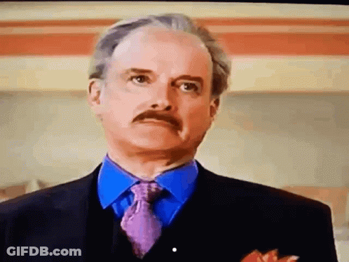 A Man With A Mustache Wearing A Suit And Tie Looks At The Camera GIF