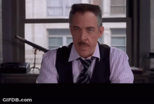 A Man With A Mustache Wearing A Vest And Tie Looks At The Camera GIF