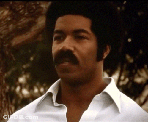 A Man With A Mustache Wearing A White Shirt Looks At The Camera GIF