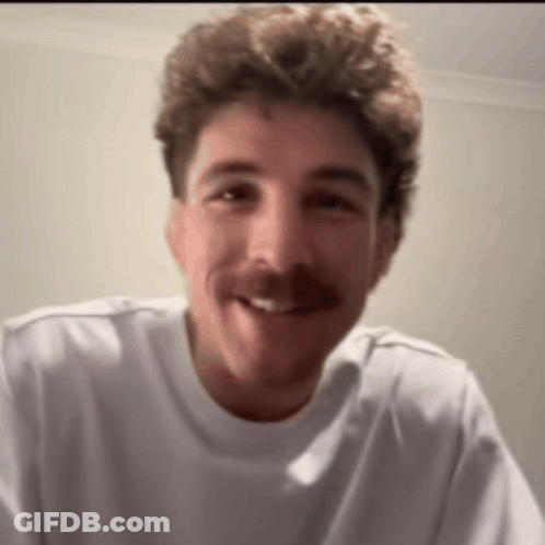 A Man With A Mustache Wearing A White Shirt Smiles For The Camera GIF