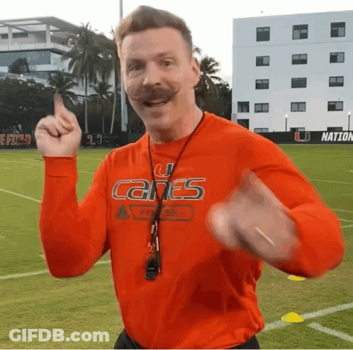 A Man With A Mustache Wearing An Orange Shirt That Says Canes On It GIF