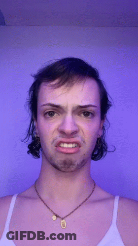 A Man With A Necklace Around His Neck Is Making A Face GIF