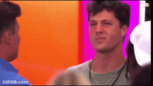 A Man With A Necklace Around His Neck Is Talking To Another Man . GIF