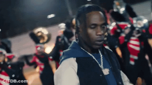 A Man With A Necklace Around His Neck Stands In Front Of A Band GIF