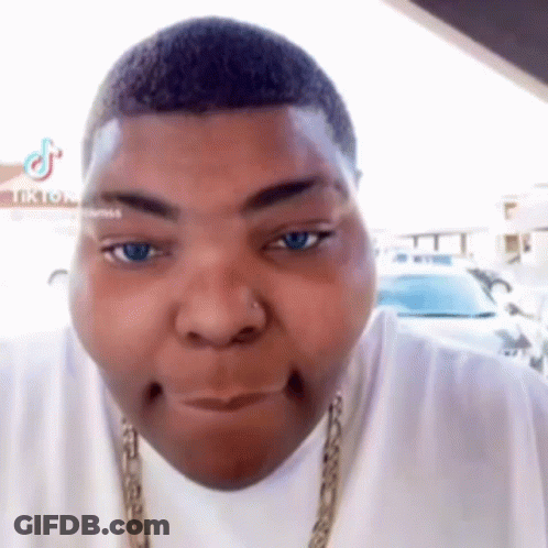 A Man With A Nose Ring Is Making A Funny Face While Wearing A White Shirt And A Gold Chain . GIF