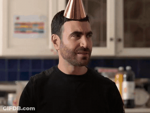A Man With A Party Hat On His Head Looks At The Camera GIF