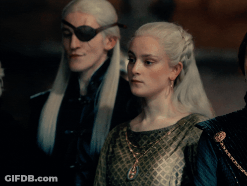 A Man With A Pirate Eye Patch And A Woman In A Green Dress Are Standing Next To Each Other GIF