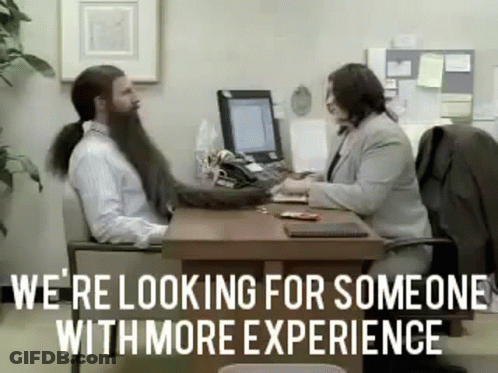 A Man With A Ponytail Is Sitting At A Desk Talking To A Woman . GIF