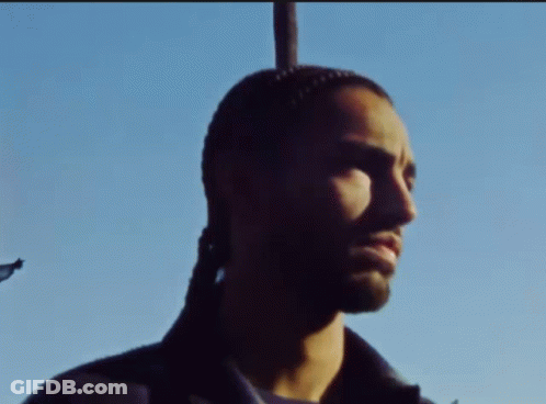 A Man With A Ponytail Is Standing In Front Of A Pole GIF