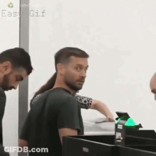 A Man With A Ponytail Is Standing Next To A Woman At A Counter . GIF