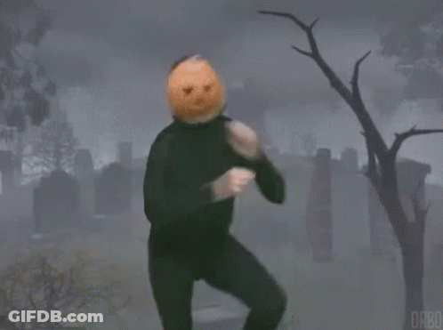 A Man With A Pumpkin On His Head Is Standing In A Cemetery . GIF