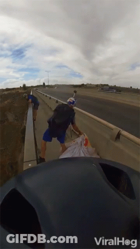 A Man With A Red Bull Helmet Is Walking Across A Highway GIF