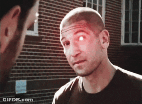 A Man With A Red Eye Is Talking To Another Man In Front Of A Brick Building GIF