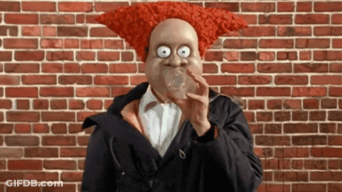 A Man With A Red Wig On His Head Blowing A Bubble GIF