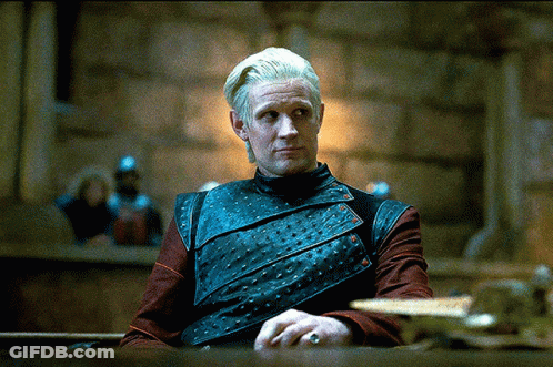 A Man With A Ring On His Finger Sits At A Table In A Dark Room GIF