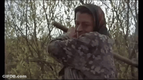 A Man With A Scarf Around His Head Is Holding A Rifle In A Field . GIF