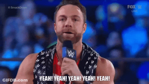 A Man With A Scarf Around His Neck Is Holding A Microphone And Saying Yeah Yeah Yeah Yeah Yeah GIF