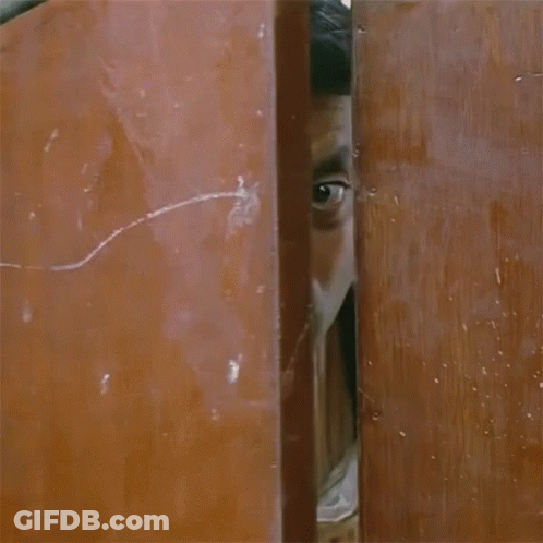 A Man With A Scarf Around His Neck Is Peeking Out Of A Doorway GIF