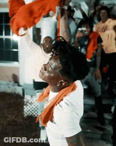 A Man With A Scarf Around His Neck Is Standing In Front Of A Crowd GIF