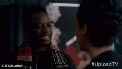 A Man With A Scarf Around His Neck Smiles While Talking To A Woman With #Uploadtv Written Below Him GIF