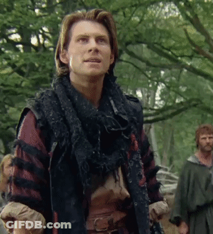 A Man With A Scarf Around His Neck Stands In The Woods GIF