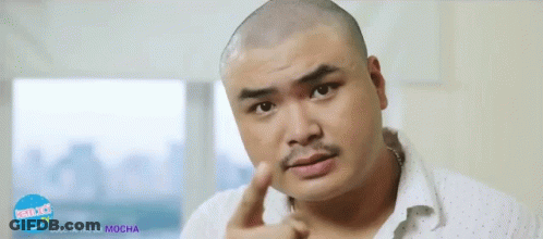 A Man With A Shaved Head And A Moustache Is Pointing At Something In Front Of A Sign That Says Mocha Tv GIF