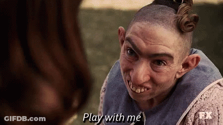 A Man With A Shaved Head And Big Teeth Is Talking To A Woman And Says `` Play With Me '' . GIF