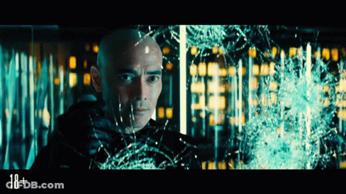 A Man With A Shaved Head Is Looking Through A Broken Glass Window With The Number 18 On The Bottom GIF
