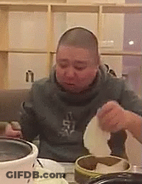 A Man With A Shaved Head Is Sitting At A Table Eating Food From A Bowl . GIF