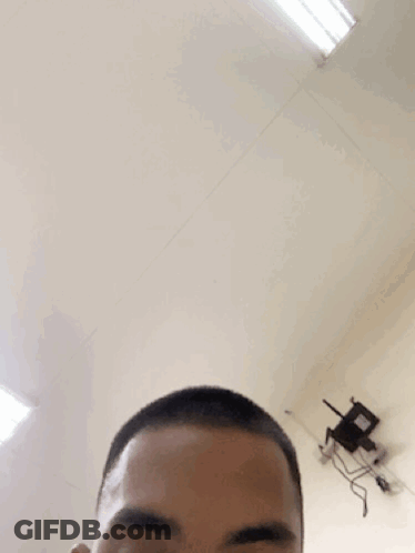 A Man With A Shaved Head Looks At The Camera With A Chair In The Background GIF