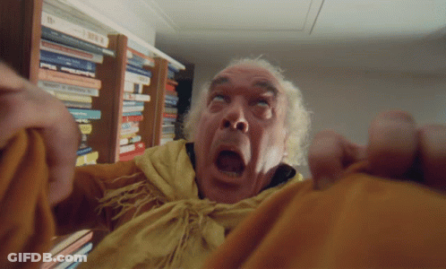 A Man With A Shocked Look On His Face Is Standing In Front Of A Bookshelf Full Of Books GIF