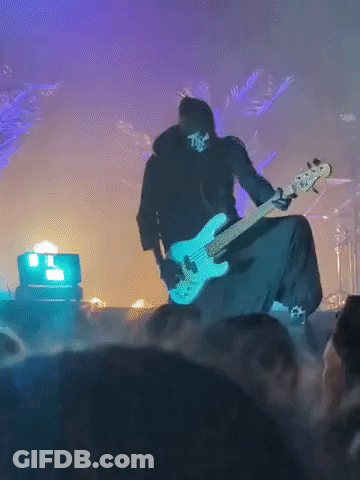A Man With A Skull On His Face Is Playing A Guitar On Stage GIF