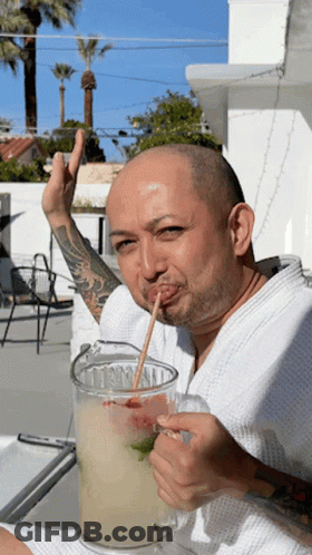 A Man With A Straw In His Mouth Drinking A Drink From A Pitcher GIF