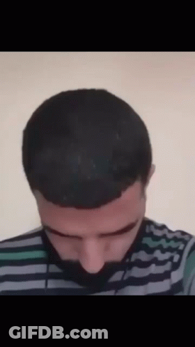 A Man With A Striped Shirt And A Beard Is Looking Down GIF