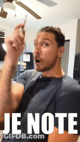 A Man With A Surprised Look On His Face Is Holding A Cell Phone In Front Of A Sign That Reads Je Note GIF