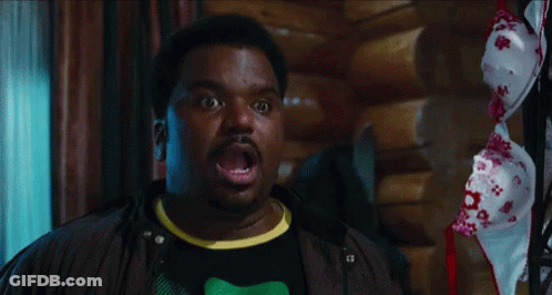 A Man With A Surprised Look On His Face Stands In Front Of A Bra Hanging On A Rack GIF