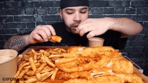 A Man With A Tattoo On His Arm Is Eating Fish And Fries GIF