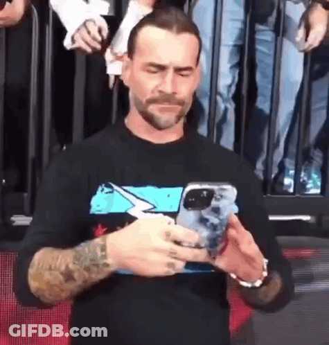 A Man With A Tattoo On His Arm Is Holding A Cell Phone . GIF