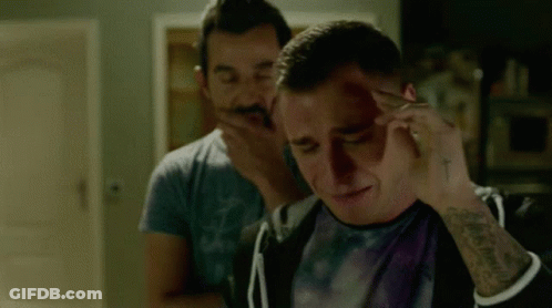 A Man With A Tattoo On His Arm Is Holding His Head While Another Man Holds His Hand To His Face . GIF