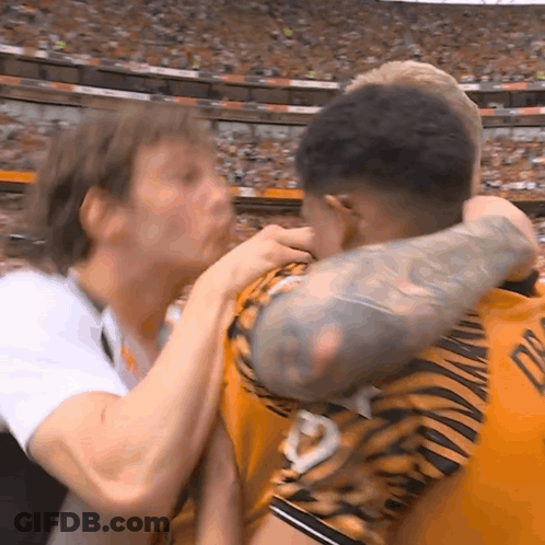 A Man With A Tattoo On His Arm Is Hugging Another Man With A Tiger Print Shirt GIF