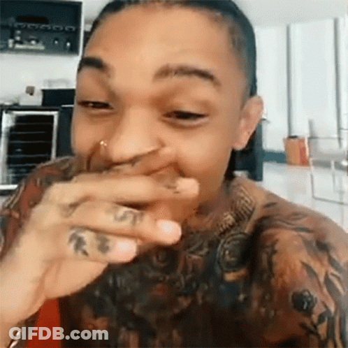 A Man With A Tattoo On His Arm Is Laughing And Covering His Mouth With His Hand . GIF