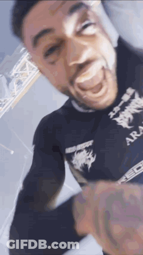 A Man With A Tattoo On His Arm Is Making A Funny Face While Wearing A Black Shirt . GIF