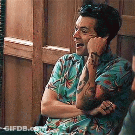 A Man With A Tattoo On His Arm Is Sitting In A Chair With His Arms Crossed And Laughing . GIF