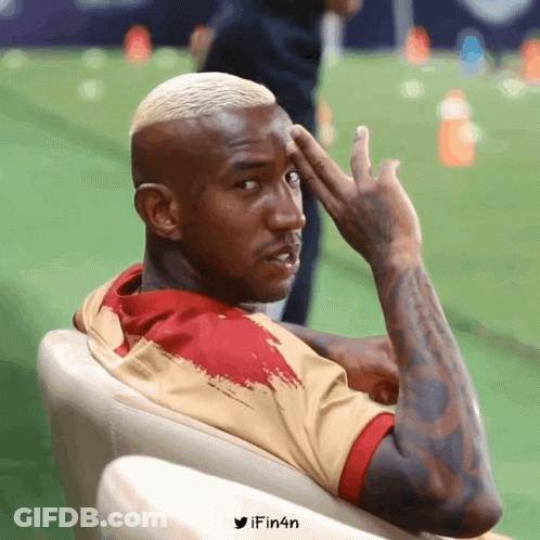 A Man With A Tattoo On His Arm Is Sitting In A Chair With His Hand On His Forehead And The Words Ifin4n Below Him GIF