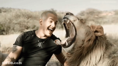A Man With A Tattoo On His Arm Is Sitting Next To A Lion With Its Mouth Wide Open GIF