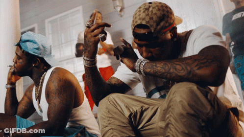 A Man With A Tattoo On His Arm Is Sitting Next To Another Man GIF