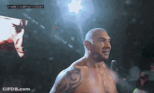 A Man With A Tattoo On His Arm Is Standing In Front Of A Screen That Says Wrestling With Text GIF