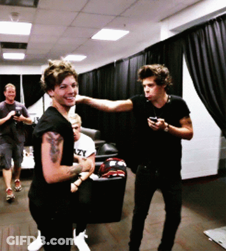A Man With A Tattoo On His Arm Is Standing Next To Another Man Who Is Holding A Cell Phone GIF