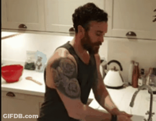 A Man With A Tattoo On His Arm Is Washing His Hands In A Kitchen GIF