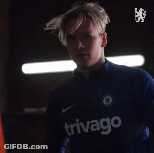 A Man With A Tattoo On His Arm Is Wearing A Blue Shirt With A Chelsea Logo On It . GIF